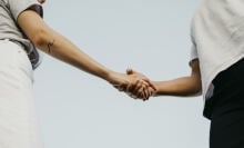 Two people shaking hands against the blue sky. 