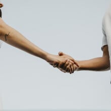 Two people shaking hands against the blue sky. 