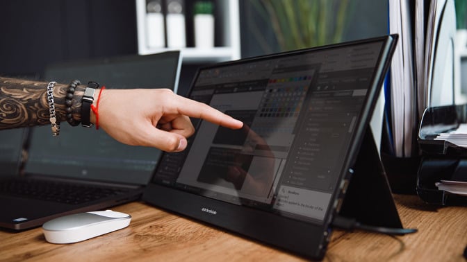 A tattooed arm reaching out to touch a touchscreen monitor 