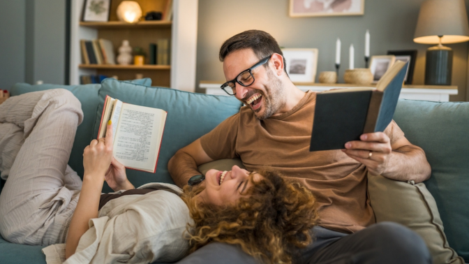 Adult couple man and woman Caucasian husband and wife in a relationship real book hold books on the sofa bed at home in the apartment reading leisure bonding family concept real people copy space