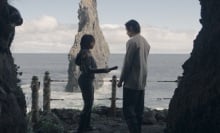 Osha holds an unlit lightsaber between her and the Stranger; the two stand at a cave entrance overlooking the ocean.