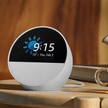 the amazon echo spot shows the time while sitting on a table with a cup of tea beside it