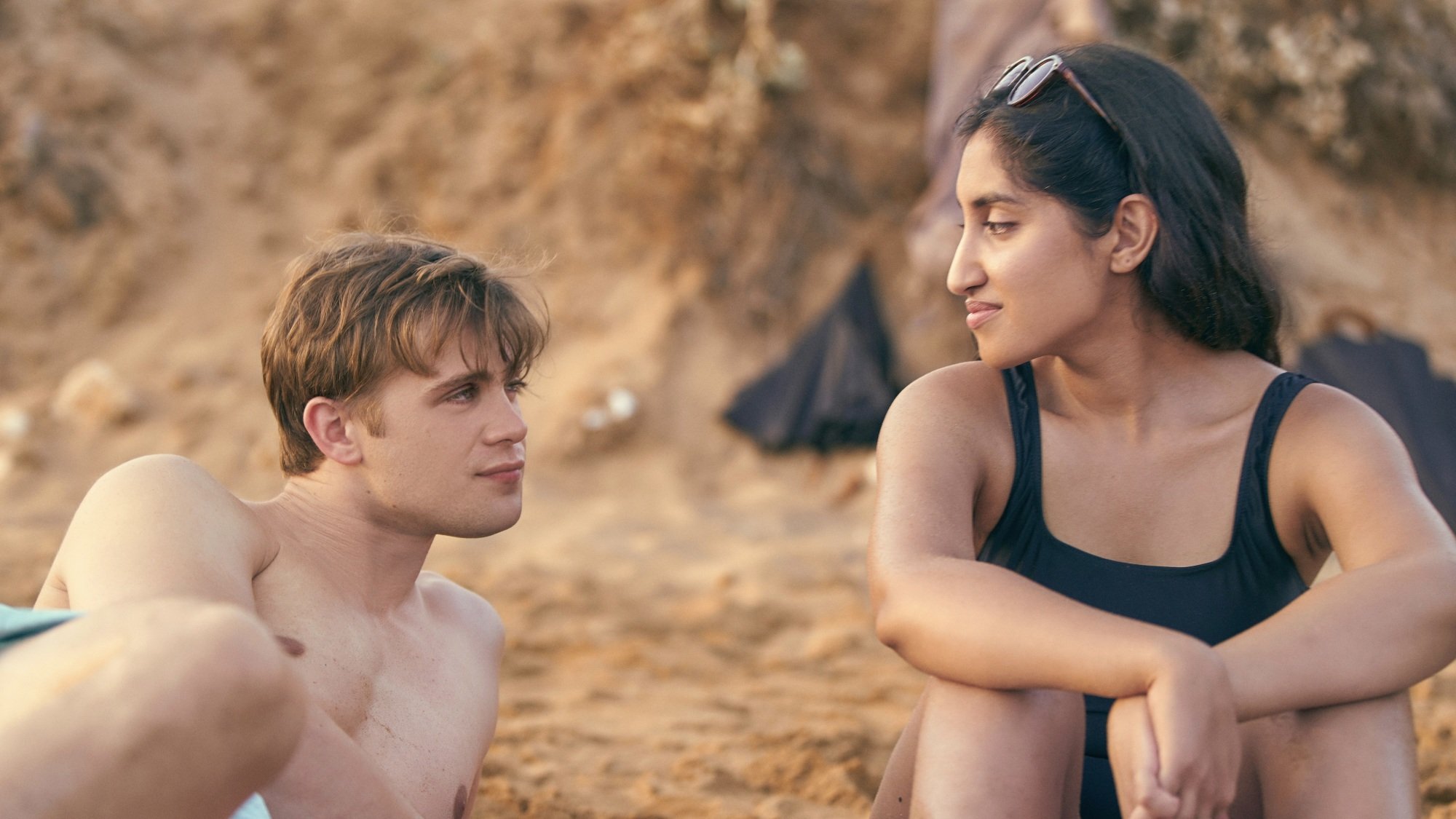 A man and woman look at each other while at a beach.