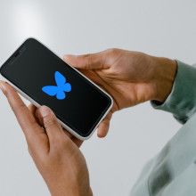 Bluesky logo on a smartphone held in someone's hands.