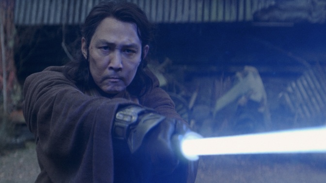 Jedi Master Sol extends his blue lightsaber towards an unseen enemy.