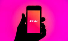 Silhouette of a hand holding a smartphone displaying the Tinder app.