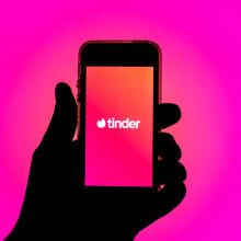 Silhouette of a hand holding a smartphone displaying the Tinder app.