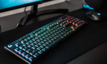 Logitech G915 wireless gaming keyboard on a desk in front of a gaming PC