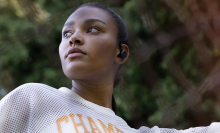 A woman jogger wearing Skullcandy earbuds in her ears while looking thoughtfully off to the side