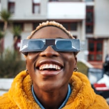 a woman using eclipse glasses to view the eclipsing sun