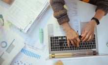 A person has financial paperwork out while working on a computer.