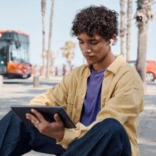 Boy sits outside using a tablet and JBL Tune 230 earbuds 