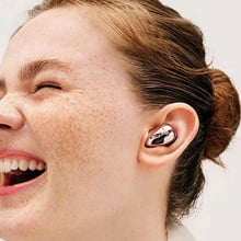 Woman with freckles smiling while wearing the Samsung Galaxy Buds Live in one ear.