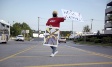 An ALU member stands in the median of a road holding a sign that reads "Honk 4 Unions."