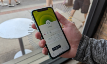 a close-up of a man holding an iphone displaying the expressvpn app in front of a window