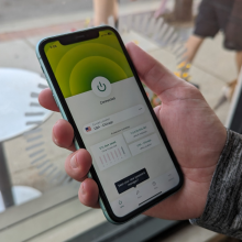 a close-up of a man holding an iphone displaying the expressvpn app in front of a window