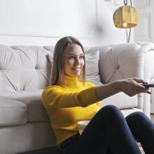 blonde woman wearing a yellow sweater pointing a remote control at a television