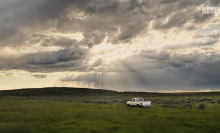 A truck drives through New Mexico with the sun shining through the clouds.