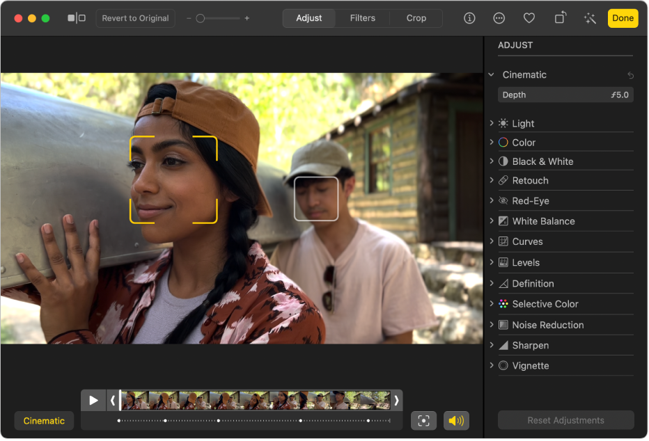 A video in editing view with a frame viewer below. A yellow box around a person’s face on the screen shows the subject currently in focus; a gray box shows another possible subject. The Cinematic button and Play button are to the left of the frame viewer, and the Toggle Focus button and Audio button are on the right. The Adjust pane is open on the right showing adjustment options.