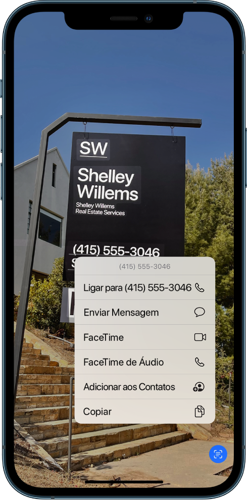 Uma foto está aberta ocupando a tela inteira. Na foto há uma placa que contém um texto e um número de telefone. O número de telefone está selecionado e as opções seguintes estão disponíveis na tela: Ligar, Enviar Mensagem, FaceTime, FaceTime de Áudio, Adicionar aos Contatos e Copiar.