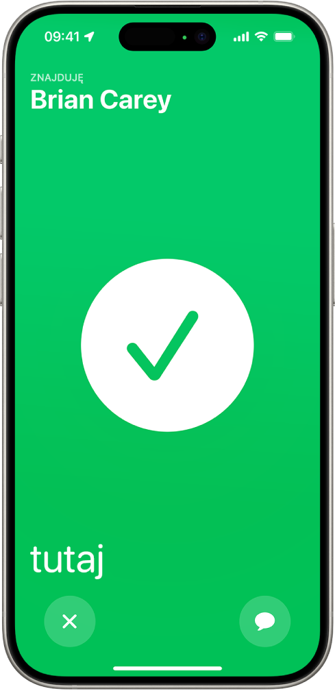 Ekran iPhone’a mający kolor zielony. Na środku widoczna jest duża ikona zaznaczenia. W lewym górnym rogu wyświetlane jest imię lokalizowanej osoby. W lewym dolnym rogu znajduje się etykieta „tutaj”, oznaczająca, że udało się spotkać.