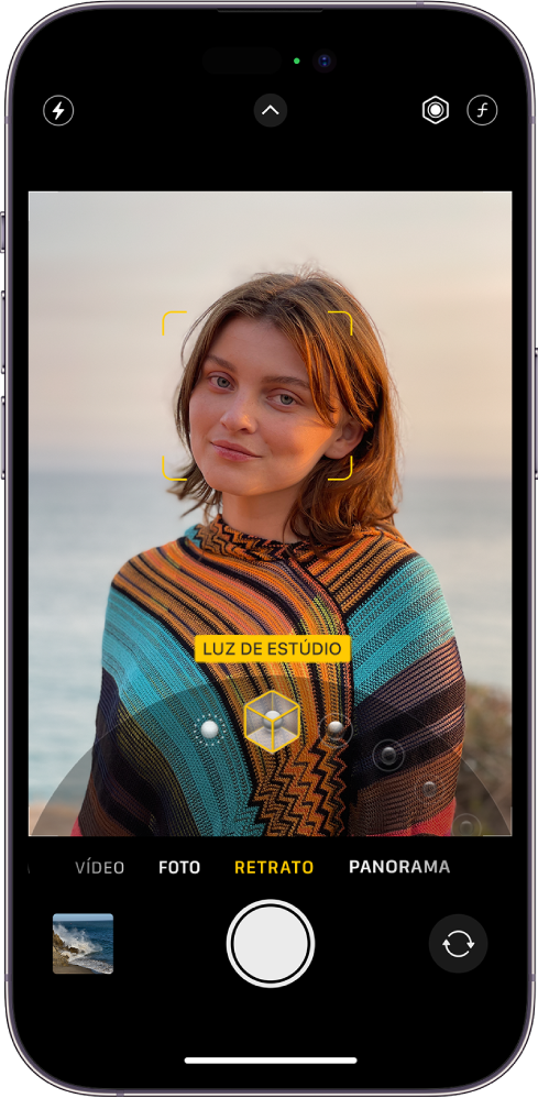 Tela do app Câmera no modo Retrato; no visor, o tema está nítido e o fundo está desfocado. O botão para escolher a Iluminação de Retrato é exibido na parte inferior da moldura e a opção Luz de Estúdio está selecionada. No canto superior esquerdo da tela está o botão Flash, na parte superior central o botão Controles da Câmera e, no canto superior direito, os botões para ajustar a intensidade da Iluminação de Retrato e o Controle de Profundidade. Na parte inferior da tela estão, da esquerda para a direita, o botão Visualizador de Foto e Vídeo, o botão Tirar Foto e o botão Seletor de Câmera Traseira.