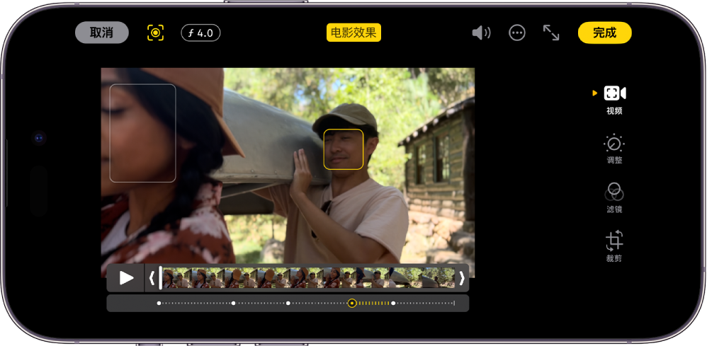 横排“电影效果”模式视频的“编辑”屏幕。屏幕左上方是“取消”按钮、“电影效果手动”按钮和“景深调整”按钮。屏幕顶部中间的“电影效果”按钮已选中。屏幕右上方是“音量”按钮、“更多选项”按钮、“进入全屏幕”按钮和“完成”按钮。视频位于屏幕中间，对焦主体周围显示外框。视频下方是画格检视器，显示视频中主体焦点变化的点。屏幕右侧的编辑按钮从上到下依次为：“视频”、“调整颜色”、“滤镜”和“裁剪”。