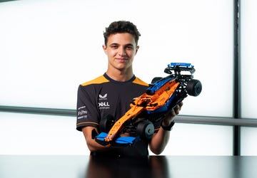 formula 1 driver lando norris smiles as he holds the lego technic mclaren f1 car, product id number lego 42141