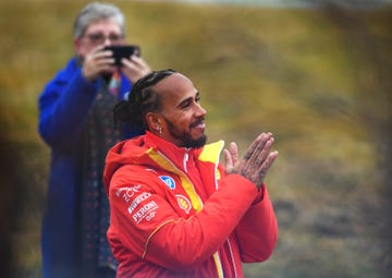 lewis hamilton smiles and raises his hands in appreciation of ferrari fans, as his mum proudly takes a photograph of him using her mobile phone