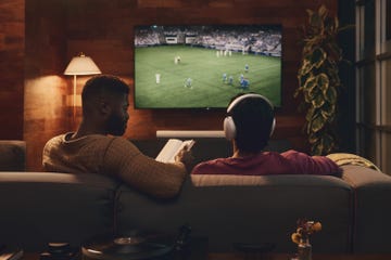 people sat on a sofa watching a football match with headphones