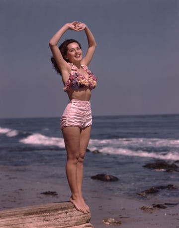 young woman in flowered top bathing suit standing on a rock at oceans edge