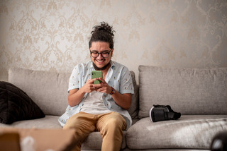 Homem se diverte enquanto utiliza um smartphone no sofá