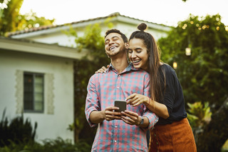 Casal demonstra felicidade enquanto utiliza um aparelho celular