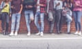 Group of eight teen friends on their phones in front of brick wall background. 