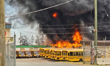 Smoke and flames rise above parked yellow busses