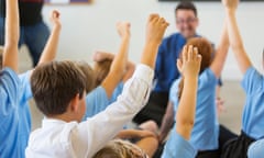 Excited schoolchildren in class with hands up.