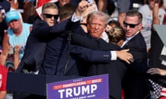 Donald Trump gestures with a bloodied face while he is assisted by Secret Service personnel after he was shot in the right ear during a campaign rally in Butler, Pennsylvania