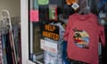 black sign with 'help wanted' in orange letters displayed on a store window around clothes and other signs