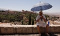 A tourist shades himself beneath an umbrella at San Nicolas viewpoint in front of La Alhambra