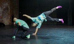 Two male dancers on stage, one about to do a handstand or flip, with his feet in the air