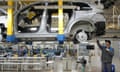 A worker assembling a car frame that is raised above the floor of the factory