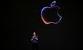 man wearing blue shirt with hands together stands in front of black screen with Apple logo