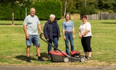 Four middle-aged people stand on a freshly mown grassy area with a mower beside them.