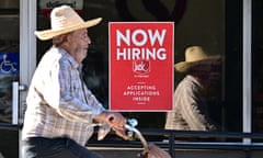 A cyclist rides past a ‘Now Hiring’ sign