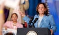 woman wearing blue suit stands at podium in front of microphone and points