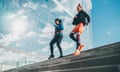 Two women jog down stairs by a modernist building.