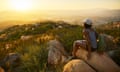 Rear view of woman hiker sitting on rock on top of hill while looking at sunset over San Diego California