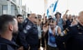 Protesters outside Sde Teiman detention facility clap and wave the Israeli flag in the face of security personnel guardian the perimeter fence