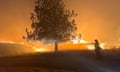 The sky is orange as a firefighter works to contain the wildfire with a hose