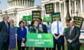 people hold green, black and yellow signs as person standing in front of podium speaks